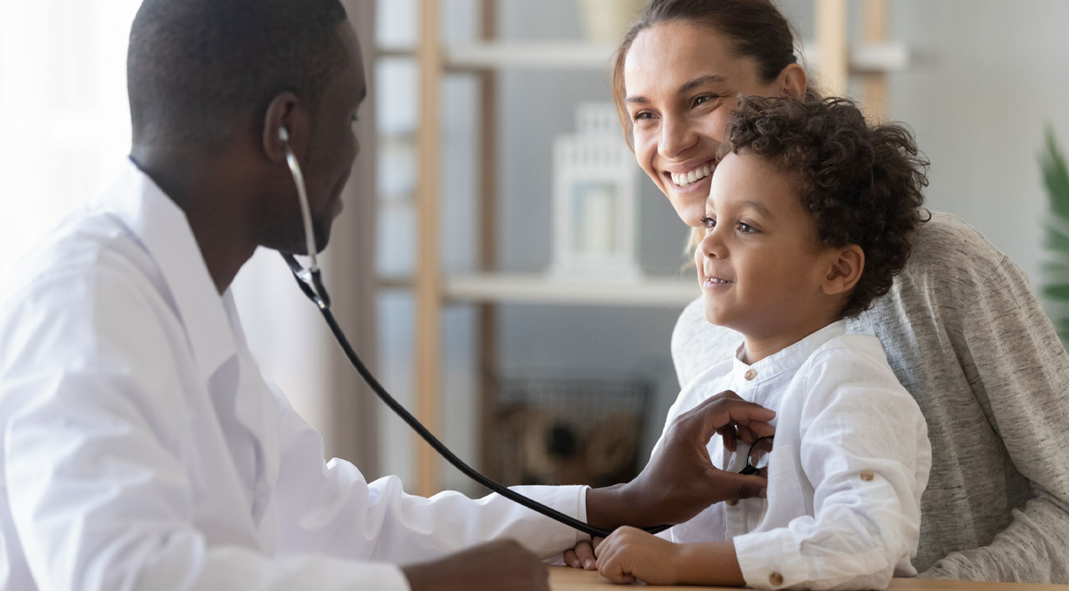 Doctor using stethoscope on son that is held by his mother.