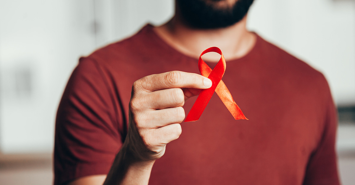 Male holding red ribbon, symbolizing HIV and AIDs awareness
