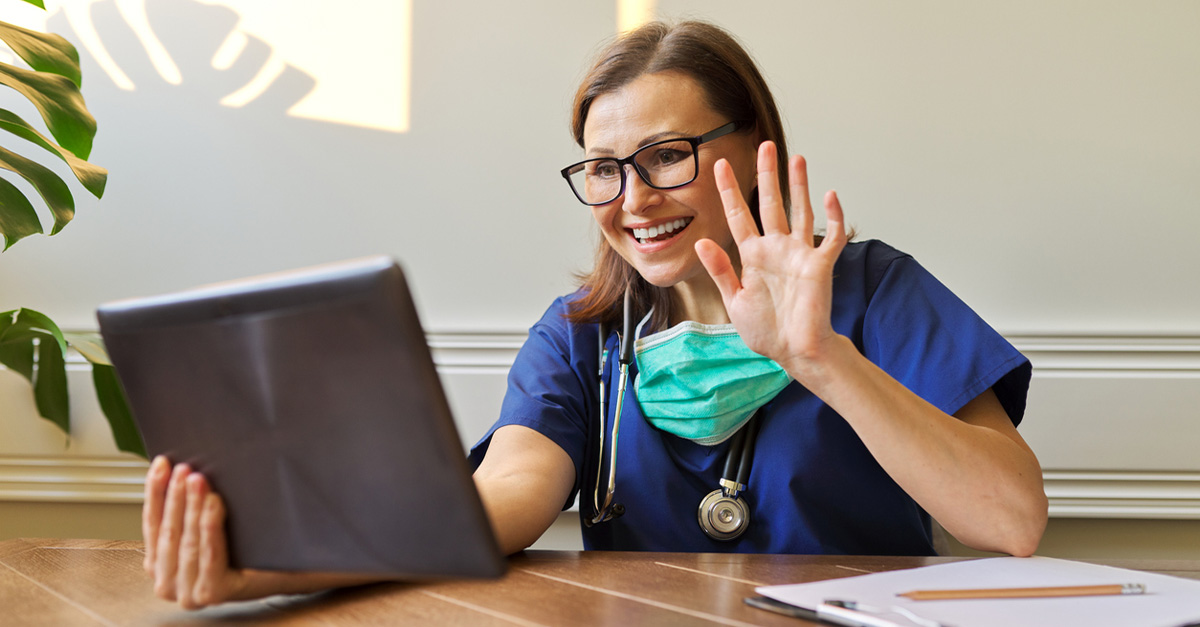 Doctor waving at patient during TeleHealth appointment, holding iPad.