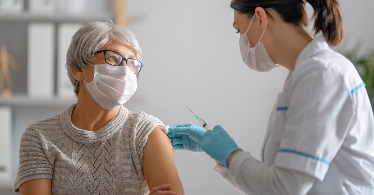 Doctor vaccinating senior woman wearing a face mask.