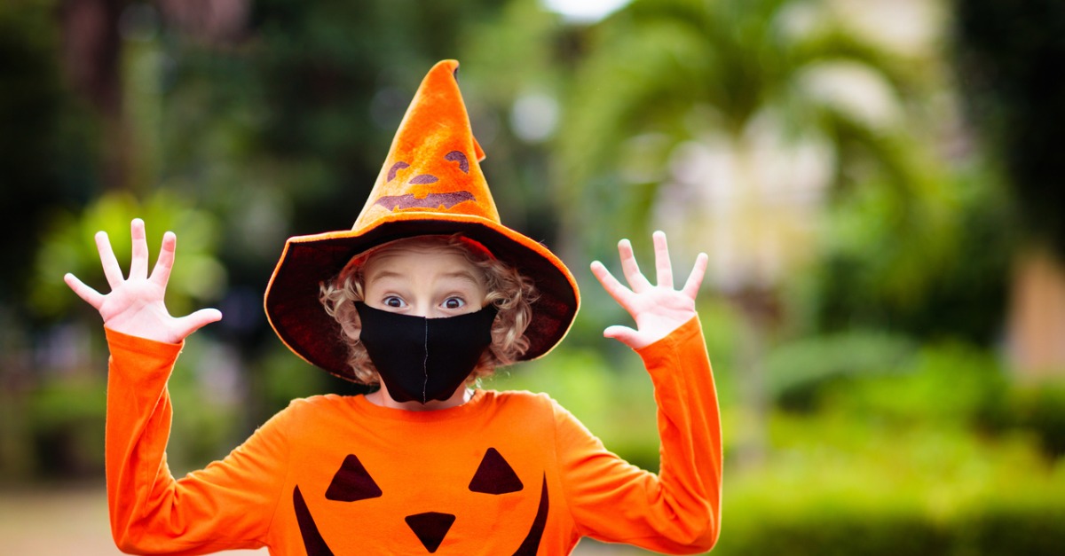 Kid dressed up as a pumpkin for Halloween while wearing a black face mask.