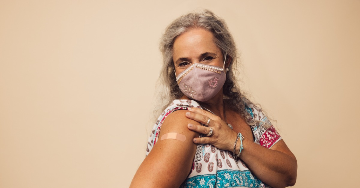 Woman wearing mask, showing bandaid where she received her COVID-19 vaccination.