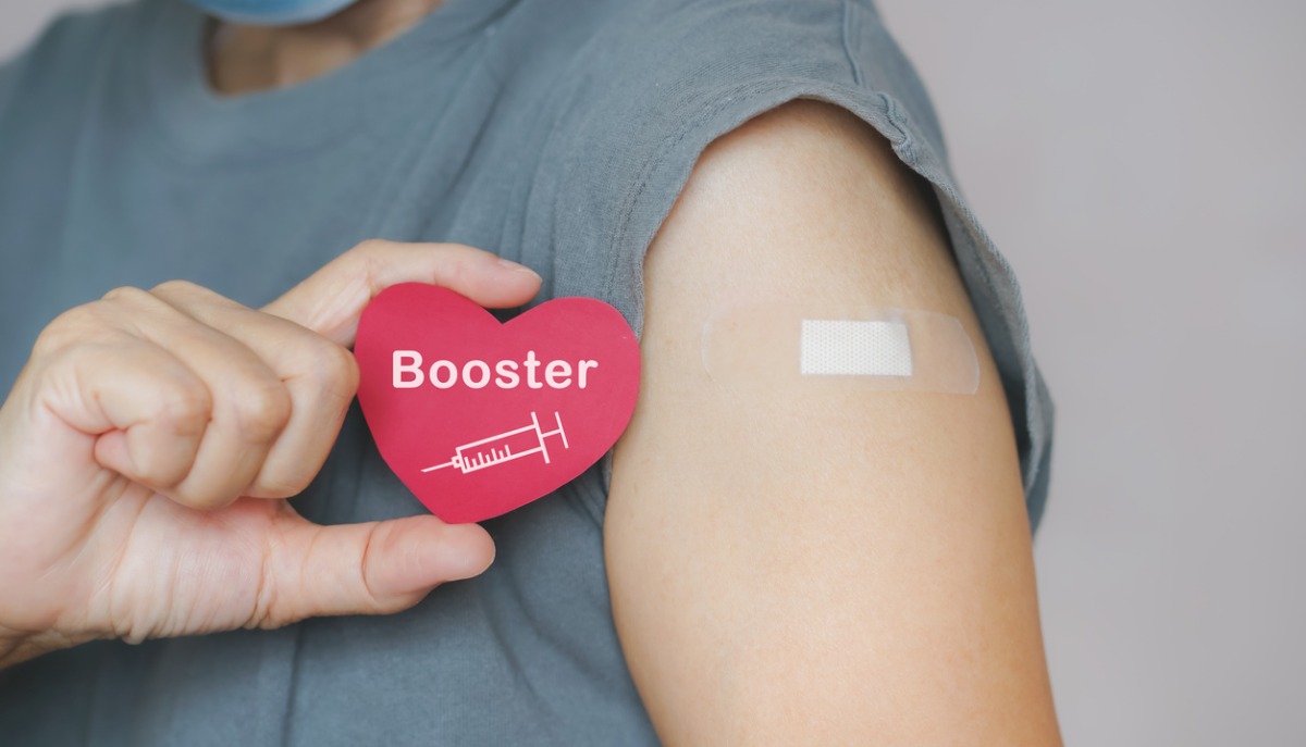 Woman holding red heart shape with syringe icon after vaccination.