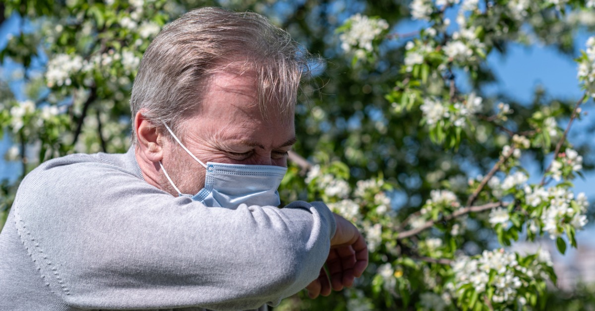 Man covering nose with shoulder while wearing mask outside, due to pollen allergies.