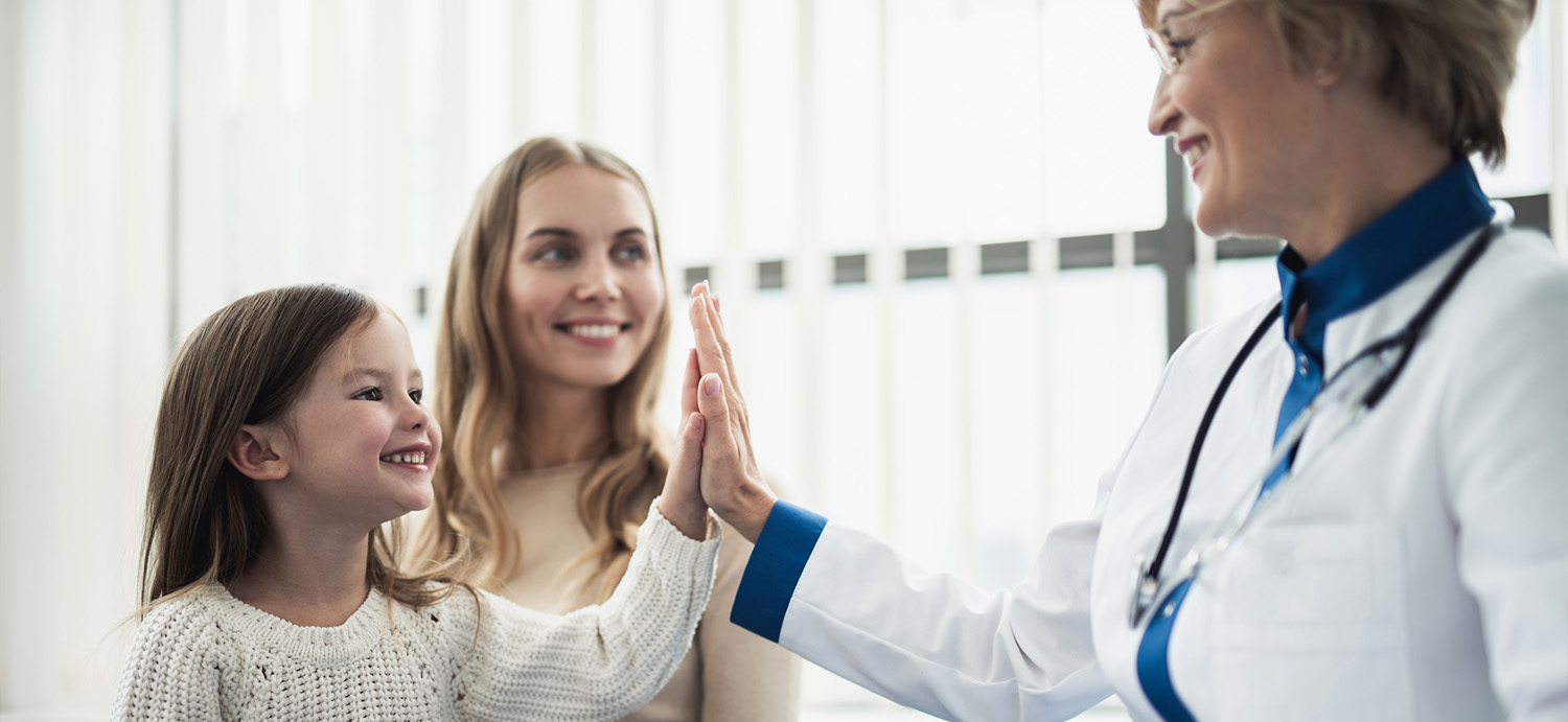 Child with mother at primary care doctor appointment, giving the female doctor a high five.
